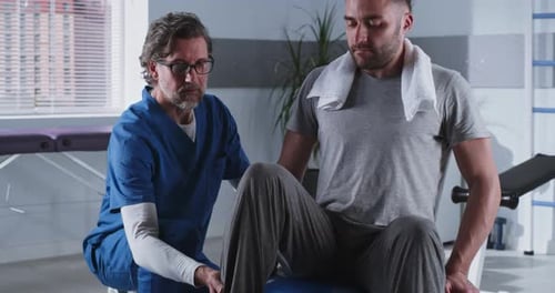 Mature Rehabilitation Therapist Helping Patient on Fit Ball