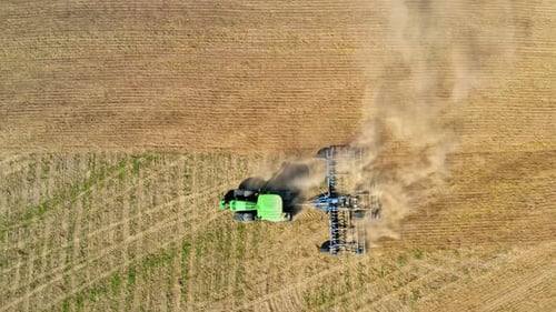 Green tractor plowing field on autumn, view from drone