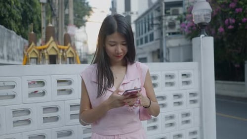 Asian Girl is Standing on the Street Laughing and Chatting on Her Mobile