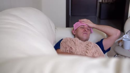 A man falls ill, lies on a couch with a severe headache