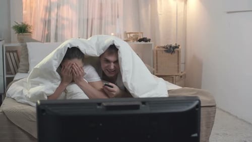 Couple Watching Scary Movie Under Blanket in Bedroom