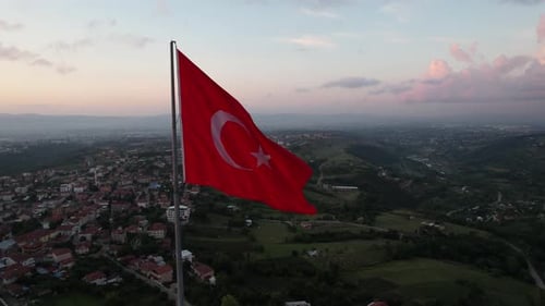 Waving Red Flag Over Green Hills at Sunset