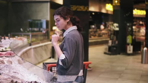 Young Female Costumer Trying to Choose Seafood at a Supermarket