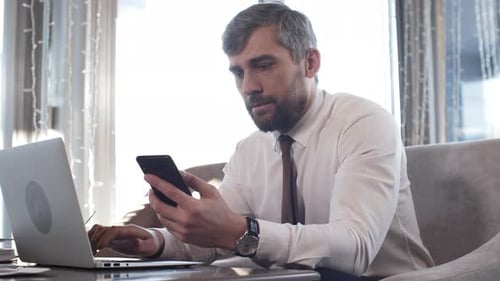 Man Works on Laptop and Cell Phone in Office