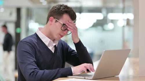 Man Working on Laptop Rubbing Eyes at Desk