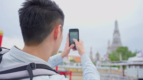 Asian man backpacker using mobile phone take picture of Buddha temple.