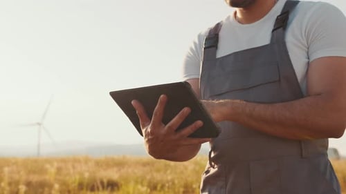 Man Using Tablet on Farm with Windmills