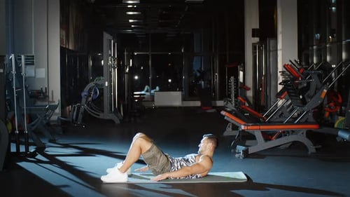 Muscular Young Man Doing Workout Heel Touch Exercises for Abs Back and Core on Floor Mat in Gym