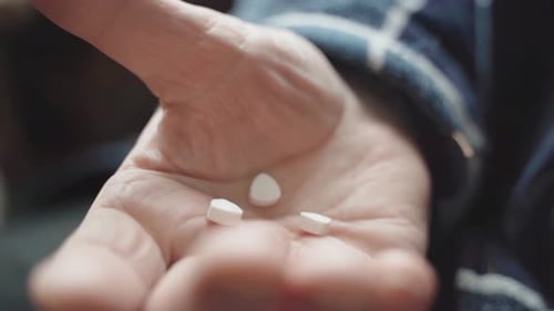 Close Up View of Senior Male Hand Holding Two Pills While Feeling Bad and Taking Treatment