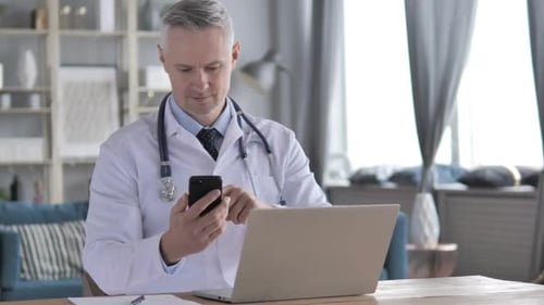 Mature Doctor Using Smartphone at Desk