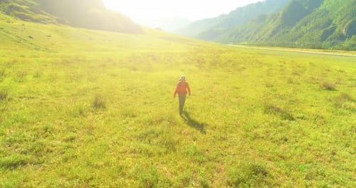 Flight Over Backpack Hiking Tourist Walking Across Green Mountain Field. Huge Rural Valley at Summer