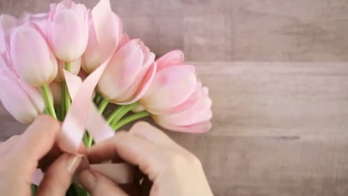 Hands Tying Pink Ribbon on Delicate Tulip Bouquet