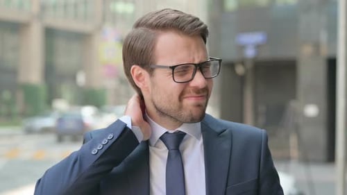 Frustrated Man Massaging Neck in Urban Setting