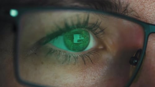 Vue macro de l'œil d'une fille portant des lunettes et regardant un écran d'ordinateur.