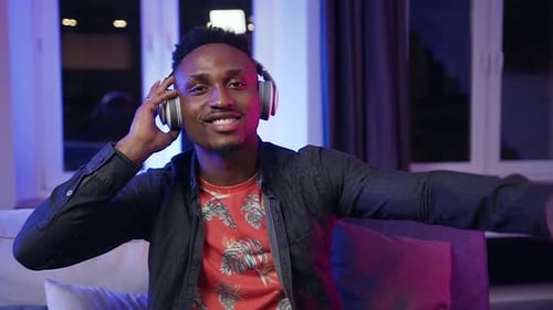 Black-Skinned Man Sitting on the Couch and Listening Inflammatory Music in His Headphones