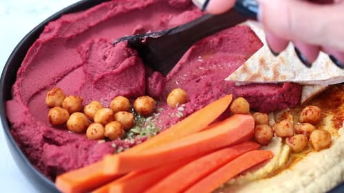 Rote-Bete-Hummus und klassischer Hummus in schwarzer Schale mit Karotten und Pitabrot.