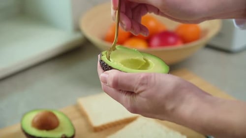 Adult scooping avocado with spoon for avocado toast