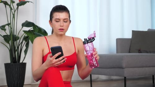 Athletic Woman Drinks Water While Using Phone