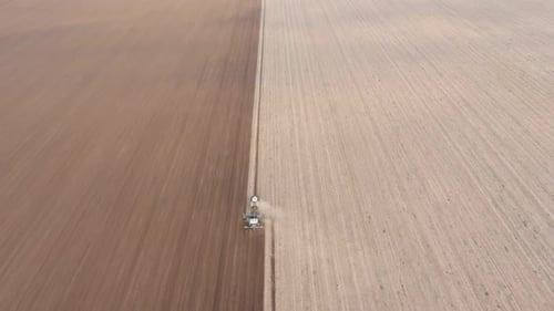 Aerial Shot of a Two Color Agriculture Field with a Tractor Furrowing It in Autumn