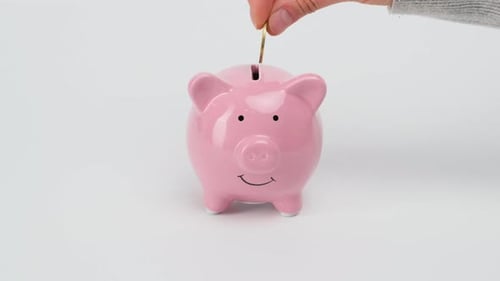Female hand puts metal coins into the slot of a pink ceramic piggy bank