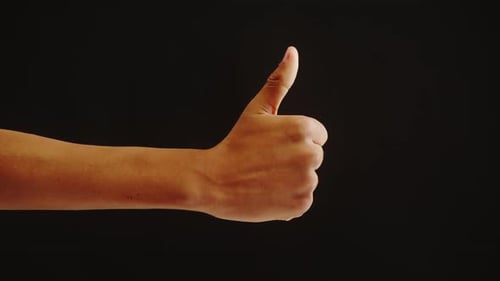 Hand Shows Thumbs Up Gesture on Dark Background