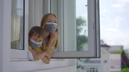 Woman and Child in Masks Looking Out Window