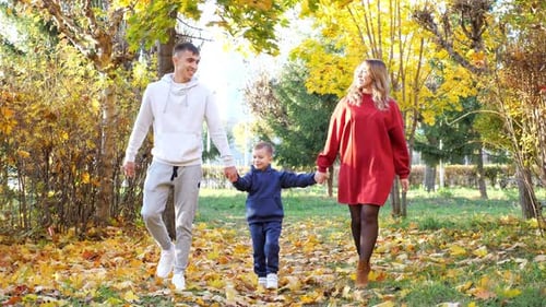 Mommy Daddy and Son Walk Joining Hands Along Autumn Park