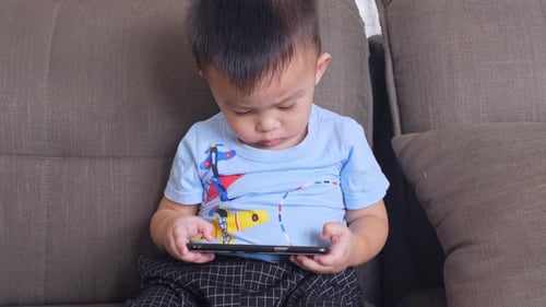 Child Plays with Smartphone on Couch at Home