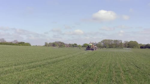Tractor Sprays Vast Green Field on Sunny Day