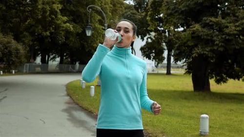 Woman Jogging and Drinking Water in Park