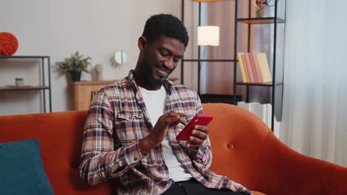 Man Smiling Using Phone on Modern Orange Couch
