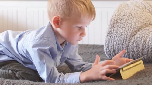 Child Lying on Bed Looking at Tablet