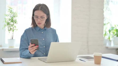 Young Woman Using Smartphone and Laptop in Office
