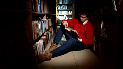 Student Sitting on Floor in Library, Reading Book. Close Up