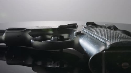 Waffenkontrolle. Studioaufnahme einer 9-mm-Pistole, die sich auf einer reflektierenden Oberfläche dreht