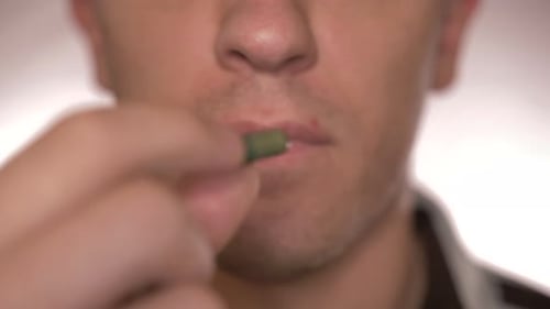 Close-up of a man eating a green pill, drinking water