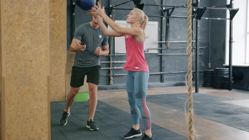 Zeitlupe von Cherful Girl Training im Fitnessstudio mit Trainer, der schwere Ballhocken wirft