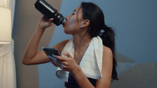 Woman Drinks Water After Workout Using Mobile Phone