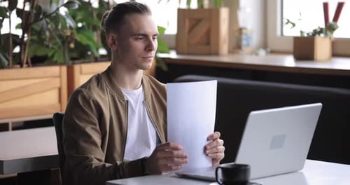 Freelancer Man Working with Papers and Laptop PC in a Cafe
