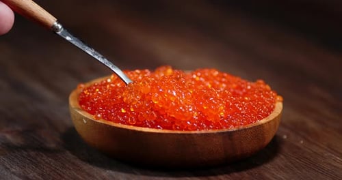 La main de l'homme avec une cuillère prend du caviar rouge dans une assiette.