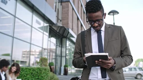 African Businessman Smiling while Browsing the Net on Tablet