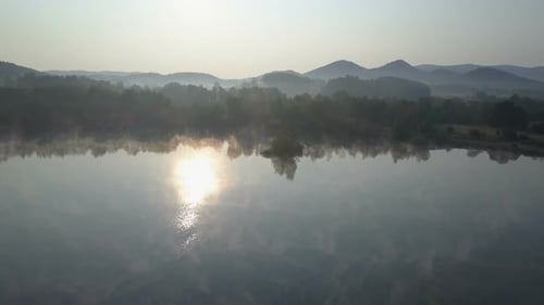 Cinematic Aerial Fly Through a Morning Fog Over a Mountain Lake. Foggy Sunrise In Mountains