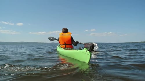 Kayaker Paddles on Calm Lake During Sunny Day