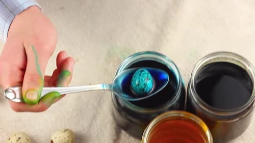 a Caucasian Child Paints a Small Easter Quail Egg in a Speck Dips It with a Metal Spoon Into Glass