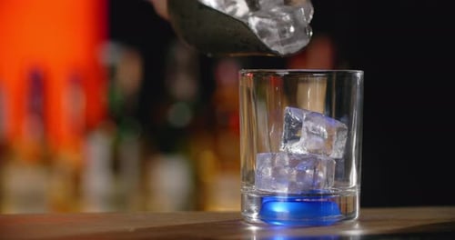Adding Ice to Glass in Dark Bar