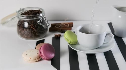 Pouring Coffee Next to Colorful Macarons and Coffee Beans