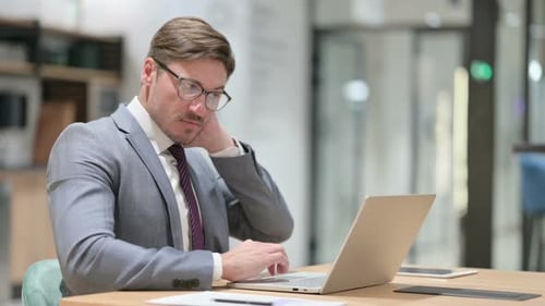 Tired Businessman with Laptop Having Neck Pain in Office
