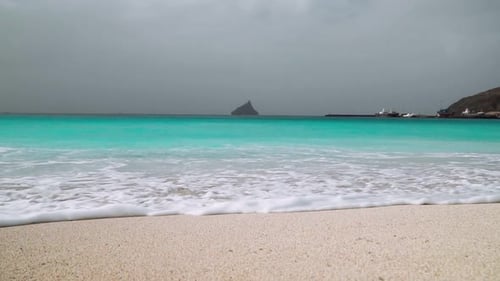 Turquoise Ocean Waves Rolling in Slow Motion to the White Sandy Beach with Huge Rock in the