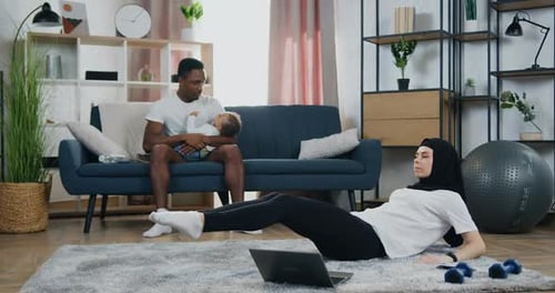 Woman Exercising as Man Holds Baby on Sofa