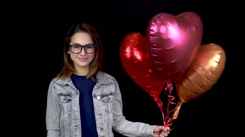 A Young Girl Is Standing with Heart-shaped Balloons. Woman Holds Helium Balls in Her Hands on a